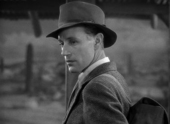 Movie still from “The Petrified Forest” (1936), directed by Archie Mayo – A black and white photo of a man wearing a hat; Close Up shot, Over the shoulder angle