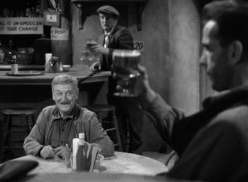 Movie still from “The Petrified Forest” (1936), directed by Archie Mayo – A man holding up a glass of beer in front of two other men sitting at a table in a restaurant; Medium shot, Over the shoulder angle