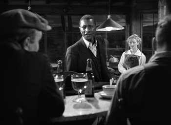 Movie still from “The Petrified Forest” (1936), directed by Archie Mayo – A black and white photo of a man sitting at a table; Medium shot, Over the shoulder angle