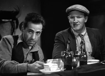 Movie still from “The Petrified Forest” (1936), directed by Archie Mayo – Two men sitting at a table in front of beer bottles; Medium shot, Low angle