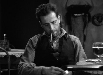 Movie still from “The Petrified Forest” (1936), directed by Archie Mayo – A black and white photo of a man smoking a cigarette; Medium shot, Low angle
