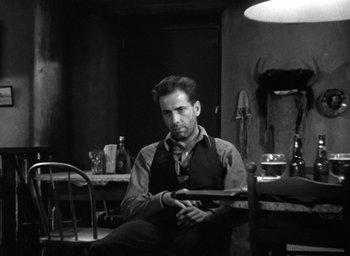 Movie still from “The Petrified Forest” (1936), directed by Archie Mayo – A black and white photo of a man sitting at a dining room table; Medium shot, Low angle