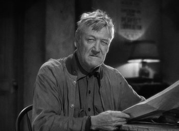 Movie still from “The Petrified Forest” (1936), directed by Archie Mayo – An older man sitting at a table holding a book; Close Up shot, Low angle