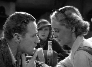 Movie still from “The Petrified Forest” (1936), directed by Archie Mayo – A man and a woman sitting in front of each other in front of a bottle; Close Up shot, Over the shoulder angle