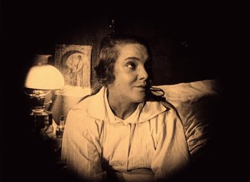 Movie still from “The Phantom Carriage” (1921), directed by Victor Sjöström – A woman sitting on a couch in front of a lamp; Medium shot, Low angle