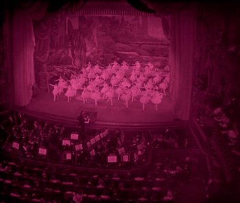Movie still from “The Phantom of the Opera” (1925), directed by Lon Chaney – An audience is sitting in front of a stage with pink lighting; Extreme Wide shot, High angle