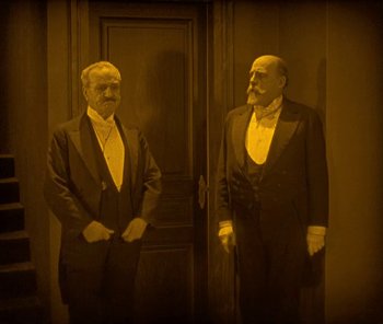 Movie still from “The Phantom of the Opera” (1925), directed by Lon Chaney – A couple of men standing next to each other in front of a door; Medium shot, High angle