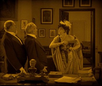 Movie still from “The Phantom of the Opera” (1925), directed by Lon Chaney – An older woman talking to two older men in an office setting; Medium shot, High angle