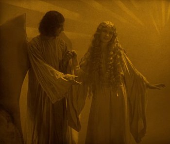 Movie still from “The Phantom of the Opera” (1925), directed by Lon Chaney – A woman in a long dress standing next to an angel; Medium shot, High angle