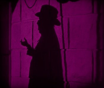 Movie still from “The Phantom of the Opera” (1925), directed by Lon Chaney – A man wearing a hat and holding a cell phone in his hand; Medium shot, Low angle