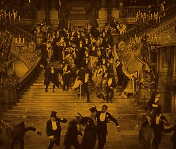 Movie still from “The Phantom of the Opera” (1925), directed by Lon Chaney – A group of men in suits and hats standing in front of a staircase; Extreme Wide shot, High angle
