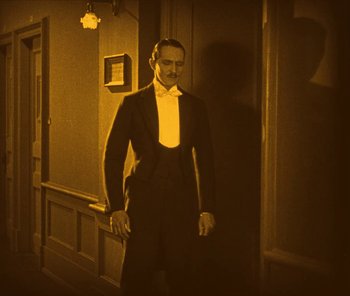 Movie still from “The Phantom of the Opera” (1925), directed by Lon Chaney – A man in a tuxedo standing next to a wall; Medium shot, Low angle