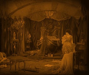 Movie still from “The Phantom of the Opera” (1925), directed by Lon Chaney – A woman sitting on a chair in front of a large statue; Extreme Wide shot, High angle
