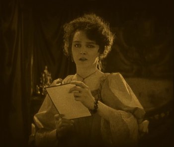 Movie still from “The Phantom of the Opera” (1925), directed by Lon Chaney – An old photo of a woman writing on a piece of paper; Medium shot, High angle
