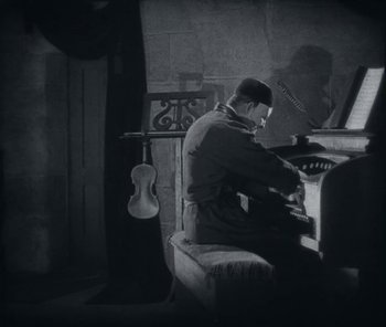 Movie still from “The Phantom of the Opera” (1925), directed by Lon Chaney – A black and white photo of a man playing a piano; Wide shot, Low angle
