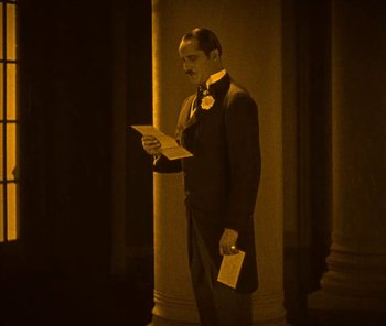 Movie still from “The Phantom of the Opera” (1925), directed by Lon Chaney – A man standing in front of a pillar holding papers; Medium shot, High angle