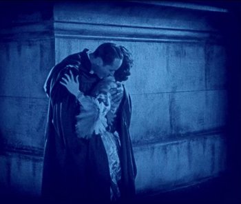 Movie still from “The Phantom of the Opera” (1925), directed by Lon Chaney – A man and a woman kissing in front of a stone wall at night; Medium shot, Low angle