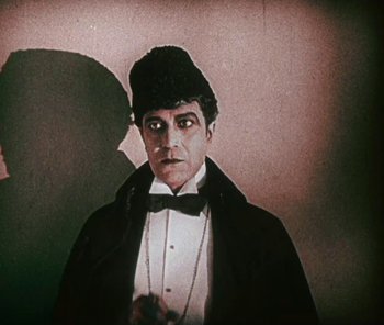 Movie still from “The Phantom of the Opera” (1925), directed by Lon Chaney – A man wearing a hat and bow tie; Medium shot, Low angle