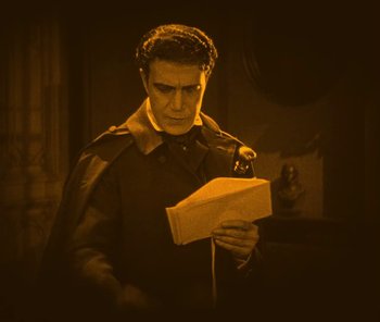 Movie still from “The Phantom of the Opera” (1925), directed by Lon Chaney – A man holding a book in his hands; Medium shot, High angle