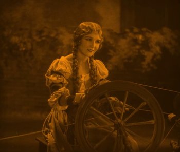 Movie still from “The Phantom of the Opera” (1925), directed by Lon Chaney – A woman in a dress sitting in front of a spinning wheel; Medium shot, High angle