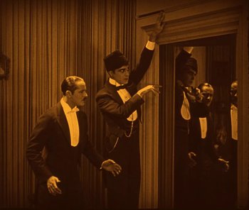 Movie still from “The Phantom of the Opera” (1925), directed by Lon Chaney – A group of men standing next to each other in a room; Medium shot, High angle