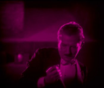 Movie still from “The Phantom of the Opera” (1925), directed by Lon Chaney – A man in a suit and bow tie smoking a cigarette; Medium shot, High angle