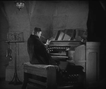 Movie still from “The Phantom of the Opera” (1925), directed by Lon Chaney – A man sitting at a pipe organ in a room; Medium shot, High angle