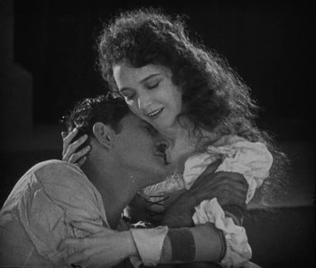 Movie still from “The Phantom of the Opera” (1925), directed by Lon Chaney – A man and a woman embracing each other in a black and white photo; Medium shot, High angle
