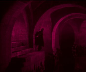 Movie still from “The Phantom of the Opera” (1925), directed by Lon Chaney – A man standing in a dark room next to a staircase; Wide shot, High angle