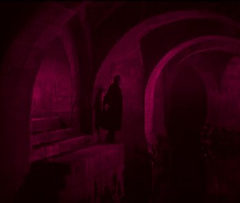 Movie still from “The Phantom of the Opera” (1925), directed by Lon Chaney – A man standing in a dark room with red lighting; Wide shot, High angle