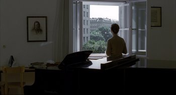 Movie still from “The Piano Teacher” (2001), directed by Michael Haneke – A woman sitting at a piano looking out a window; Wide shot, Over the shoulder angle