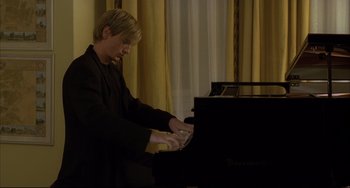 Movie still from “The Piano Teacher” (2001), directed by Michael Haneke – A man playing a piano in front of a window; Medium shot, Low angle