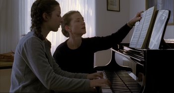 Movie still from “The Piano Teacher” (2001), directed by Michael Haneke – A woman and a young girl are playing a piano together; Medium shot, Low angle