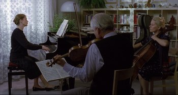 Movie still from “The Piano Teacher” (2001), directed by Michael Haneke – An older man playing a violin in front of a group of people; Wide shot, Over the shoulder angle