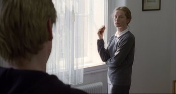Movie still from “The Piano Teacher” (2001), directed by Michael Haneke – A woman standing in front of a mirror in a room; Medium shot, Over the shoulder angle
