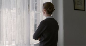 Movie still from “The Piano Teacher” (2001), directed by Michael Haneke – A woman standing in front of a window looking outside; Medium shot, Over the shoulder angle