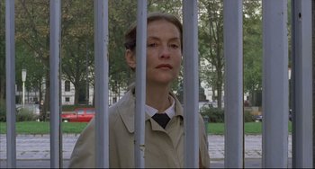 Movie still from “The Piano Teacher” (2001), directed by Michael Haneke – A woman standing behind a metal fence looking at the camera; Close Up shot, Low angle