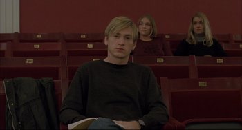 Movie still from “The Piano Teacher” (2001), directed by Michael Haneke – A man sitting in front of a woman in a lecture hall; Medium shot, Low angle
