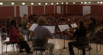 Movie still from “The Piano Teacher” (2001), directed by Michael Haneke – A group of people sitting in front of an audience playing instruments; Wide shot, High angle