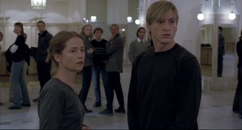 Movie still from “The Piano Teacher” (2001), directed by Michael Haneke – A group of people standing in a room; Medium shot, Over the shoulder angle