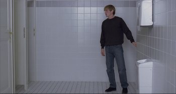 Movie still from “The Piano Teacher” (2001), directed by Michael Haneke – A man standing in front of a tiled wall in a bathroom; Wide shot, Low angle