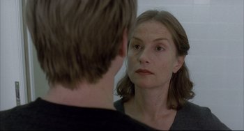 Movie still from “The Piano Teacher” (2001), directed by Michael Haneke – A woman looking into a mirror while standing next to a man; Close Up shot, Over the shoulder angle