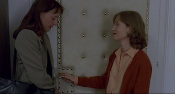 Movie still from “The Piano Teacher” (2001), directed by Michael Haneke – Two women standing next to each other in front of a wall; Medium shot, Over the shoulder angle