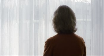 Movie still from “The Piano Teacher” (2001), directed by Michael Haneke – A woman in a red jacket is looking out a window; Close Up shot, Low angle