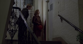 Movie still from “The Piano Teacher” (2001), directed by Michael Haneke – A woman and a man standing at the bottom of a staircase; Wide shot, Over the shoulder angle