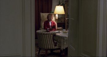 Movie still from “The Piano Teacher” (2001), directed by Michael Haneke – An older woman sitting at a table in a room; Wide shot, High angle