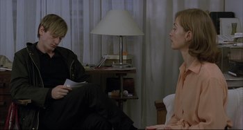 Movie still from “The Piano Teacher” (2001), directed by Michael Haneke – Two people sitting in a room with a lamp on the side of the room; Medium shot, Over the shoulder angle