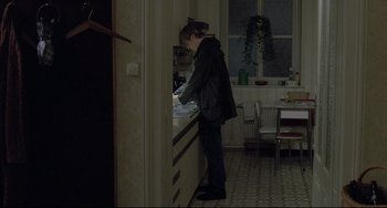 Movie still from “The Piano Teacher” (2001), directed by Michael Haneke – A person standing at a sink in a room; Wide shot, Over the shoulder angle