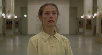 Movie still from “The Piano Teacher” (2001), directed by Michael Haneke – A woman in a white shirt is standing in an empty room; Close Up shot, Low angle