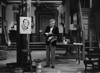 Movie still from “The Picture of Dorian Gray” (1945), directed by Albert Lewin – A black and white photo of a man holding a guitar in front of an easel; Wide shot, Low angle